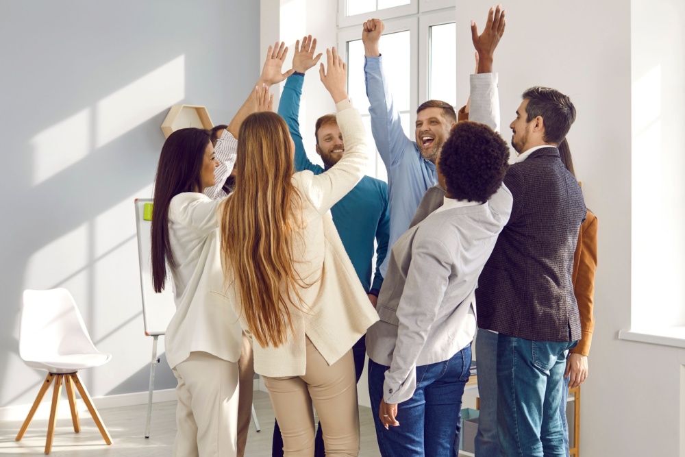 Happy people at work stand in circle and raise their hands