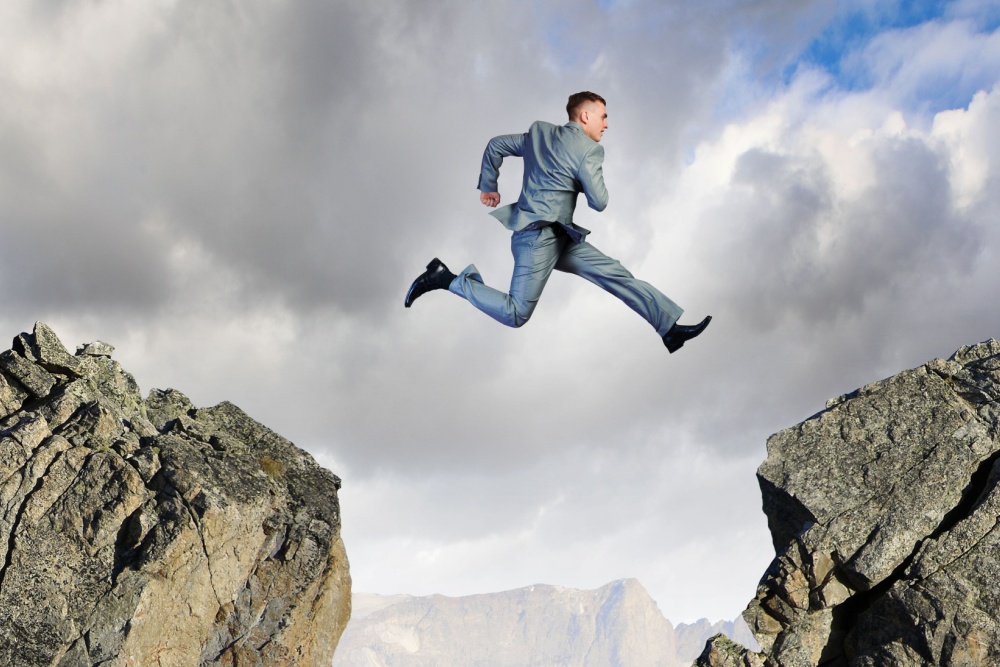 Businessman jumping over a gap between two rocks